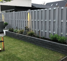 Een schutting van luxe grijze schuttingdelen en aluminium tuinpalen, waarop verlichting is aangebracht. Luxe schutting • grijs • grijs gecoat
