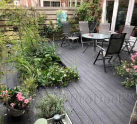 Een "wilde" tuin, met uitsparingen in het vlonder voor planten. De vlonderplanken zijn met een houtnerfreliëf, een blijvend mooie houtnerfstructuur. Vlonderplank • composiet • donkerantraciet • houtnerfreliëf