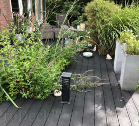 Een "wilde" tuin, waarin wat rust is aangebracht door het monteren van een donkerantracieten vlonder met houtnerfreliëf. Vlonderplank • composiet • donkerantraciet • houtnerfreliëf